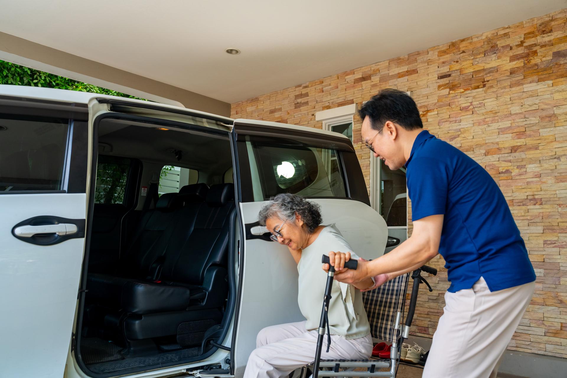 Caregiver helping senior woman get in the car.